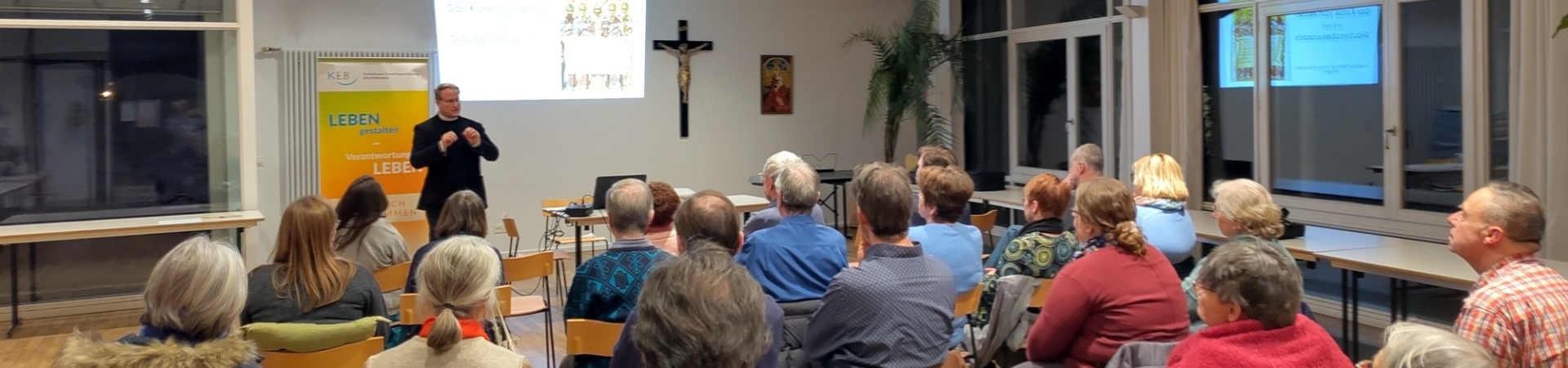 Referent spricht vor Publikum in einem Veranstaltungsraum mit Präsentation.